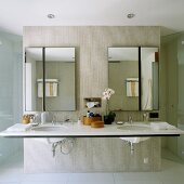 Large double washstand with asymmetrically divided mirrors on concrete partition and doors to floor-level shower on either side