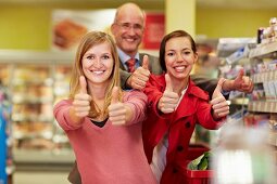 Germany, Cologne, Man and women showing thumbs up in supermarket