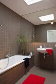 Red accents in a modern bath with a full wall mirror above the sink and brown tiles on the wall and floor