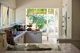 Blick über geflieste Küchenzeile in offener Küche vor Terrassentür und Blick in den Garten