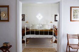 Weisses Metallbett unter quadratischem Lichtfenster; neben dem Bett zwei vergoldete Hängelampen