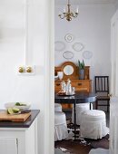 Dining room with antique sideboard and collection of china plates on wall; round dining table and upholstered stools with white loose covers in foreground