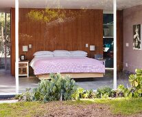 View of bed in sleeping area in glass-walled house