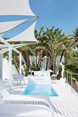 Designer sun loungers on white terrace with sunken pool below triangular awnings
