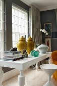 Chinese vases next to stacked books and white orchids on white table next to white stool