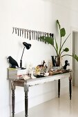 Retro table lamp next to ceramic figurines and vase of palm leaves on vintage table below collection of scissors hanging on wall