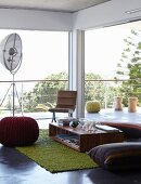 Low seating area with various floor cushions in front of glass wall encircled by terrace