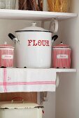 Enamel pots and tins with red lettering on vintage-style kitchen shelves