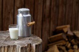 Milchkanne und Milchglas auf rustikalem Holzblock