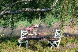 Garden table set with bundt cake and summer flowers below birch tree