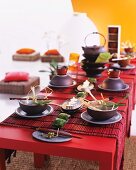 Asian place settings with floral decorations on a red table with red bamboo table runners