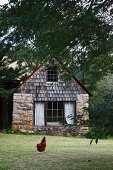 Umherlaufendes Huhn im Garten mit kleinem rustikalem Landhaus