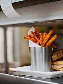 Würzige Pommes frites mit Wachspapier in einem Edelstahlbecher auf einer Restauranttheke