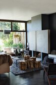 Stools made from sections of tree trunk in front of fireplace in living room with walls painted dark grey