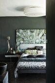Scatter cushions and bedspreads on double bed in front of modern painting on dark grey wall