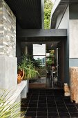 Entrance area with black tiled floor and view into foyer of contemporary house through glass door