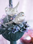 Silberglänzende Vogelfiguren und Dekoperlen auf Metallkugel