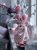 Arrangement of artificial flowers in fabric-wrapped vase on window sill