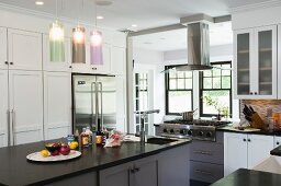 Free-standing kitchen island below modern pendant lamps with coloured glass shades in white country-house kitchen