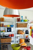 Orange industrial lamps and metal shelving in simple kitchen with colourful utensils