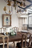 Antique wooden chairs around wooden table below multiple-armed candle chandelier in elegant, rustic dining room