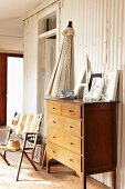 Closed sun umbrella, wooden chest of drawers and fabric lawn chair in front of white profiled sheet metal