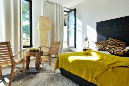 Mustard yellow bedspread on double bed with black headboard next to rustic table and chairs