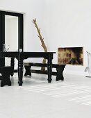 High contrasts in the living room with an antique style, black, lacquer dining table on a while tile floor. open brick fireplace and tree trunk sculpture in the corner