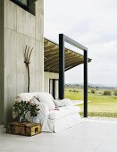 Terrace of a home located in an open landscape with an inviting sofa and crate table in front of an exposed concrete wall