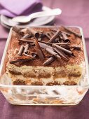 Tiramisu topped with chocolate curls, in a glass dish, part already served