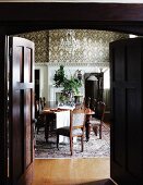 View through a dark wooden double door into a traditional dining room with a long dining table and colonial style, antique chairs