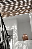 Sonneneinfall durch Bambussdach ins Treppenhaus und Blick auf Amphore in Wandnische
