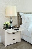 Bedside table with extendable surface and table lamp next to bed with upholstered headboard