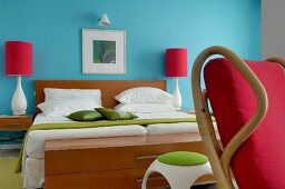Colourful, fifties-style bedroom; double bed against turquoise wall and bedside lamps with red lampshades