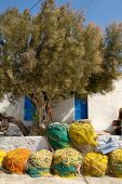 Colourful, rolled fishing nets and old tree in front of Mediterranean terrace of house with blue shutters