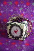 Wrapped Christmas present with reindeer motif standing on purple wrapping paper with pattern of stars