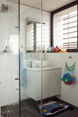 Verglaster Duschbereich neben Waschtisch mit weißem Unterschrank in Badezimmerecke unter dem Fenster