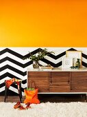 Orange colour gradient on wall above black and white zigzag dado as dynamic background for designer sideboard