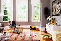 Junge auf Stuhl mit Bilderbuch und verstreutes Spielzeug in elegantem Fenstererker mit grau getönter Wand