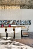 Designer dining area with cantilever chairs at a long table and mirror strips on the back wall; decorative lighting from the exposed concrete ceiling