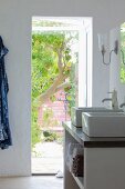 Vanity with two raised sinks and open shelves next to an open patio door with a view into a summer garden