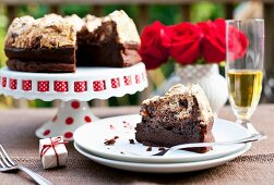 Schokoladen-Haselnuss-Kuchen mit Baiserhaube auf Kuchenständer und Teller, rote Rosen in einer Vase