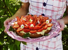 A woman holding a strawberry cake with vanilla cream
