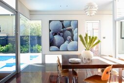Glass-walled dining room with view of pool in garden and picture of grapes on back wall