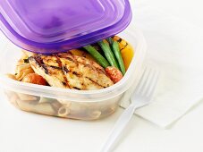 A barbecued chicken breast with vegetables and penne pasta in a food storage box