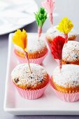 Muffins dusted with icing sugar and decorated with frilled cocktail sticks made from paper cake cases