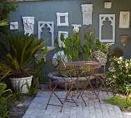 Delicate, metal outdoor furniture and potted plants on terrace in front of stylised antique frames on grey exterior wall