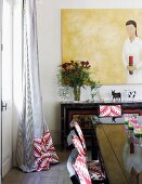 Chairs upholstered in eye-catching ethnic fabric around black glossy dining table and painting above painted sideboard