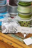 Wrapped present with name tag on silver moose-antler ornament in front of stacked spools of ribbon