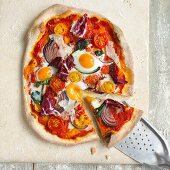 Pizza mit Wachtelei, roten Zwiebeln, Parmesan und Radicchio, angeschnitten